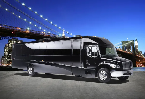 A black luxury charter bus parked in front of the Manhattan Bridge and New York City skyline at night.