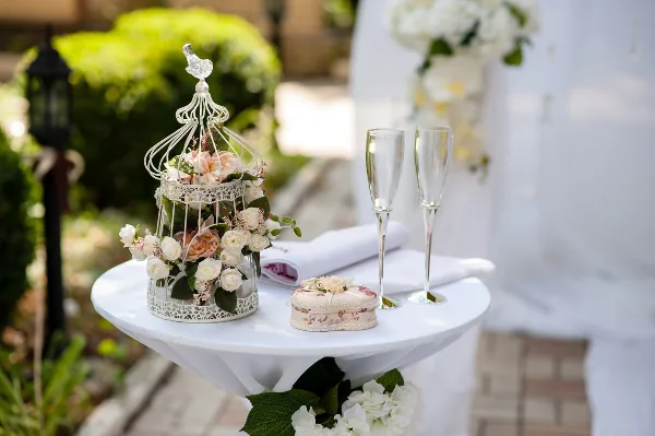 A white round table set with a tablecloth, two champagne flutes, and a decorative birdcage centerpiece filled with flowers.