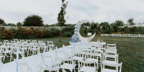 An outdoor wedding ceremony setup featuring white chairs, a floral arch, and a white aisle runner on a grassy lawn.