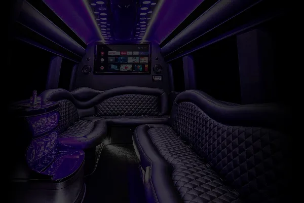 Interior view of a luxury party bus with quilted leather seating and a large entertainment screen.