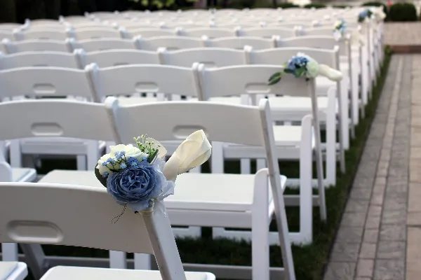 Rows of white folding chairs arranged for an outdoor wedding ceremony, decorated with floral accents.