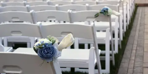Rows of white folding chairs arranged for an outdoor wedding ceremony, decorated with floral accents.