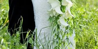 Bride in a white lace gown holding a cascading white calla lily bouquet in a grassy field