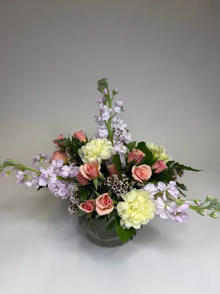 A floral arrangement with pink roses, white stock, and greenery in a glass vase.