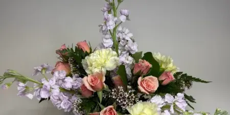 A floral arrangement with pink roses, white stock, and greenery in a glass vase.