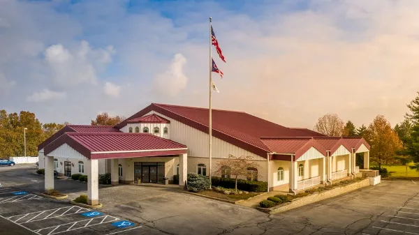 Exterior view of a large event center building with a red roof and white siding, featuring a parking lot and flagpole.