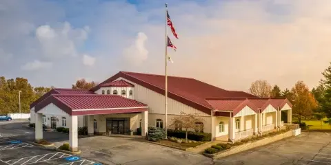 Exterior view of a large event center building with a red roof and white siding, featuring a parking lot and flagpole.