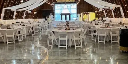 Interior of a wedding venue barn featuring a high wooden ceiling, string lights, and round tables set for a reception.