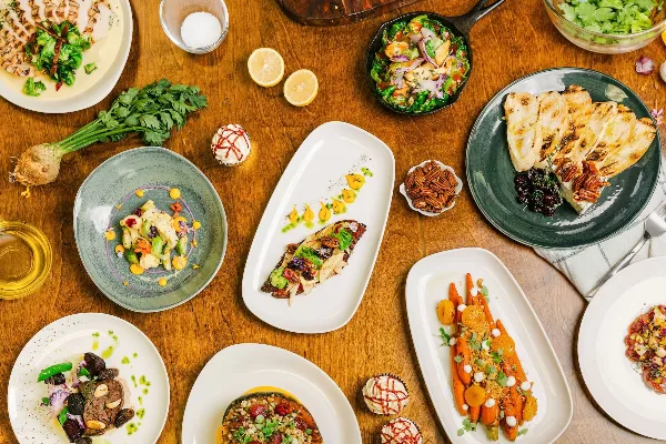 Overhead view of a wooden table filled with various plated gourmet dishes, fresh herbs, and garnishes.