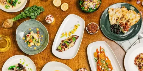 Overhead view of a wooden table filled with various plated gourmet dishes, fresh herbs, and garnishes.