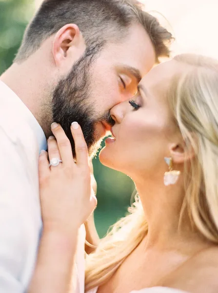 A close-up, warm-toned photograph of a bride and groom sharing an intimate moment, with the bride's hand gently touching the groom's face.