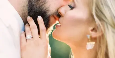 A close-up, warm-toned photograph of a bride and groom sharing an intimate moment, with the bride's hand gently touching the groom's face.