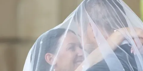 A bride and groom embracing under a white wedding veil in a candid portrait.