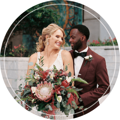 A bride and groom standing together, with the bride holding a large, colorful bouquet of flowers.