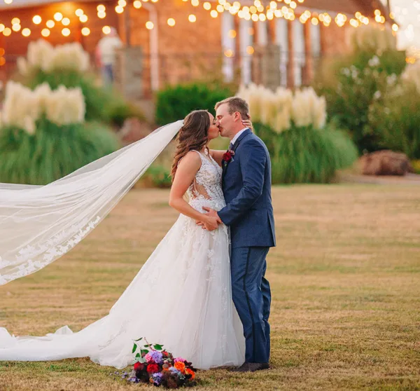 A bride and groom sharing a kiss in a garden setting with string lights in the background.