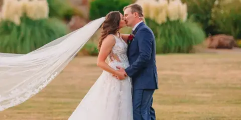 A bride and groom sharing a kiss in a garden setting with string lights in the background.