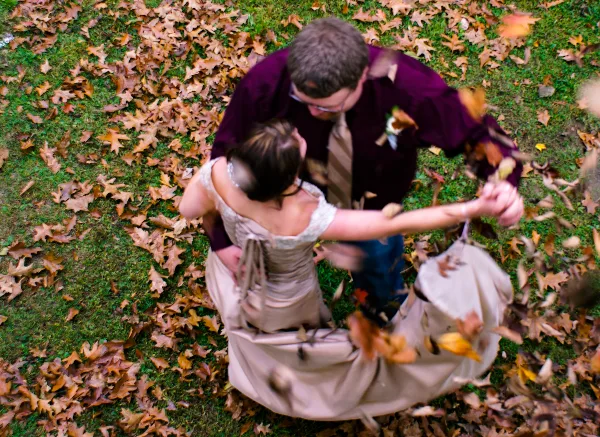 A bride and groom dancing in a field of fallen autumn leaves.