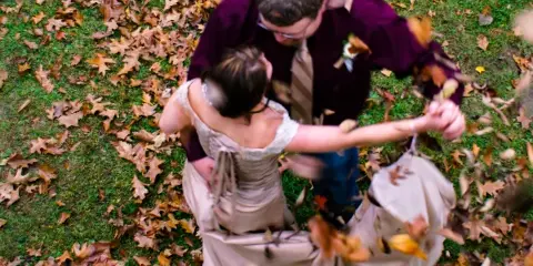 A bride and groom dancing in a field of fallen autumn leaves.
