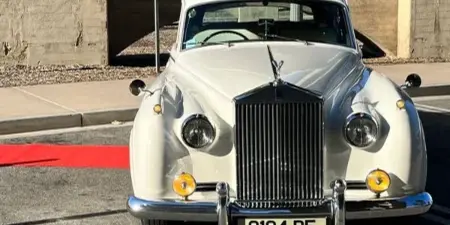 A classic silver Rolls-Royce parked outdoors in bright sunlight.