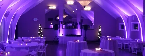 A wedding reception hall with a DJ booth, speakers, and purple ambient lighting.