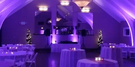 A wedding reception hall with a DJ booth, speakers, and purple ambient lighting.