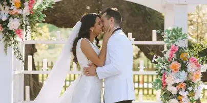 A bride and groom sharing a kiss at a white wooden ceremony arch decorated with floral arrangements on the grounds of Chatsworth Plantation.