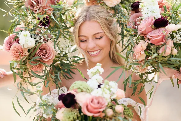 A smiling bride holding a large floral bouquet with pink and white flowers.