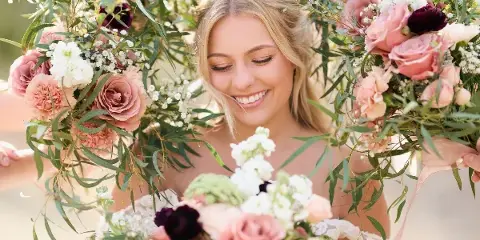 A smiling bride holding a large floral bouquet with pink and white flowers.