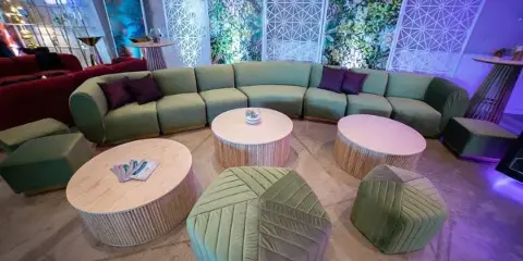 A modern lounge setup featuring a green sectional sofa, matching ottomans, and round coffee tables arranged in an event space.