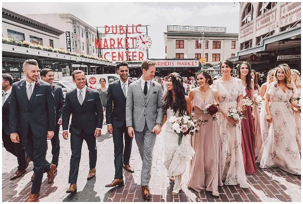 A wedding party walking on a brick street in front of the Seattle Public Market Center sign.