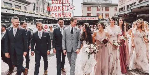 A wedding party walking on a brick street in front of the Seattle Public Market Center sign.