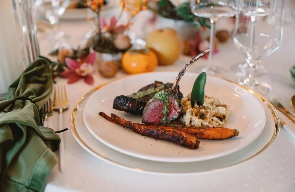 A plated meal of rack of lamb with rice and roasted carrots on a formal dining table.
