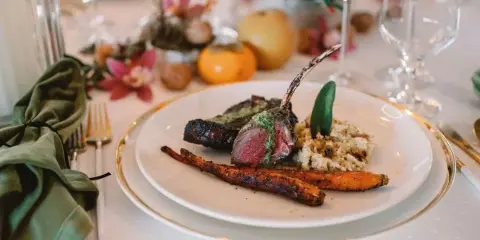 A plated meal of rack of lamb with rice and roasted carrots on a formal dining table.