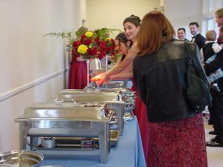 A catering station with chafing dishes and a server serving guests at an event.
