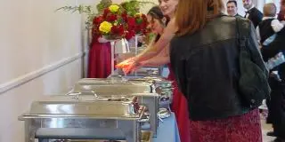 A catering station with chafing dishes and a server serving guests at an event.