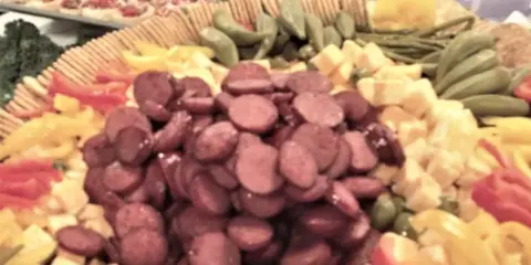 A catering platter featuring sliced sausage, cheese, and vegetables.
