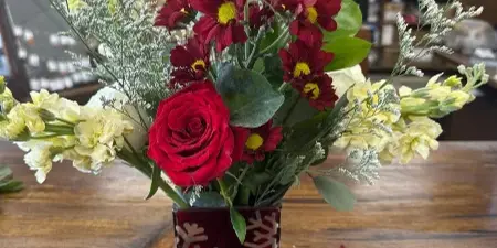 A fresh floral arrangement with red roses and chrysanthemums in a red patterned glass vase on a wooden table.