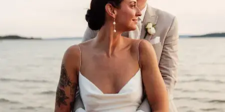 A bride and groom embracing on a beach at sunset, with the groom kissing the bride's forehead.