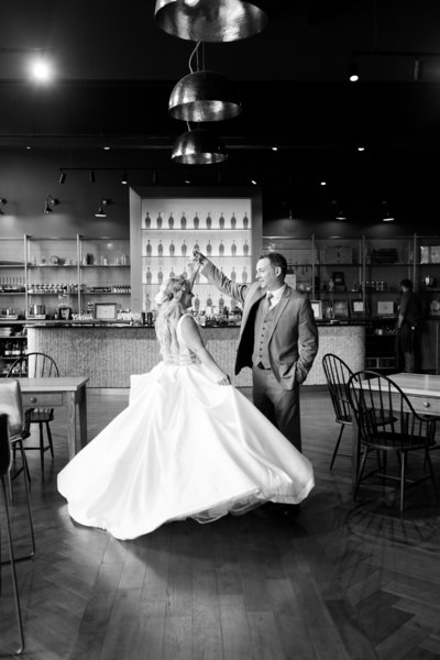 A bride and groom dancing in a black and white photograph inside a venue with a bar in the background.
