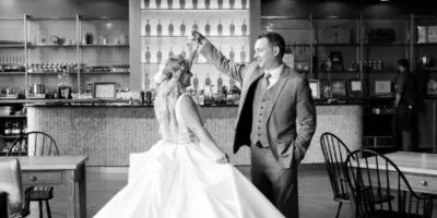 A bride and groom dancing in a black and white photograph inside a venue with a bar in the background.