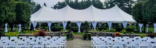 A large white event tent set up outdoors with rows of white chairs and decorative blue draping.