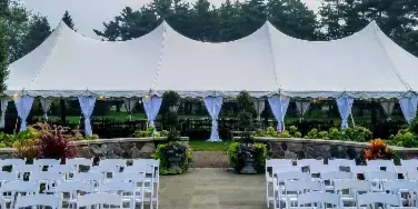 A large white event tent set up outdoors with rows of white chairs and decorative blue draping.
