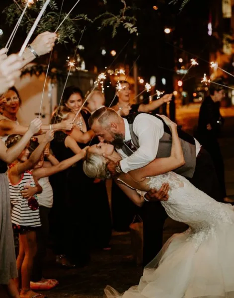 A bride and groom sharing a kiss during a sparkler exit at a wedding reception, surrounded by guests.