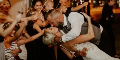 A bride and groom sharing a kiss during a sparkler exit at a wedding reception, surrounded by guests.