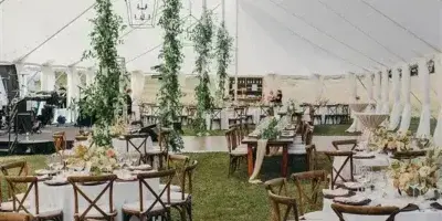 Interior view of a white wedding tent with round tables, wooden chairs, and hanging geometric lanterns.