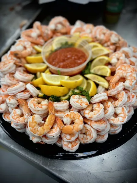 A large platter of shrimp cocktail garnished with lemon wedges and a central container of red cocktail sauce.