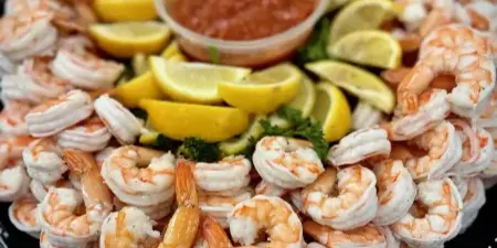 A large platter of shrimp cocktail garnished with lemon wedges and a central container of red cocktail sauce.