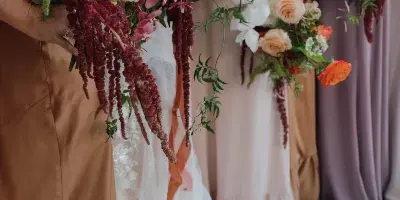 Close-up of a vibrant bridal bouquet and bridesmaids' bouquets featuring red roses, orange blooms, and trailing greenery held by the wedding party.