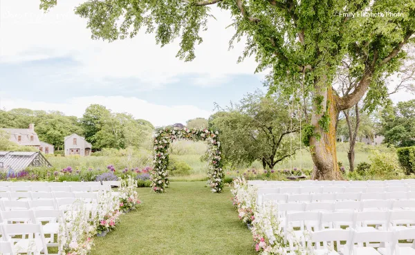 Outdoor wedding ceremony setup with a floral arch and aisle decor.