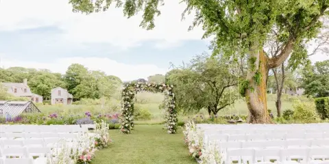 Outdoor wedding ceremony setup with a floral arch and aisle decor.